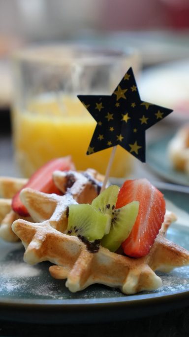 Waffel mit frischen Früchten und einem Sternen-Deko-Topper, im Hintergrund Saft.