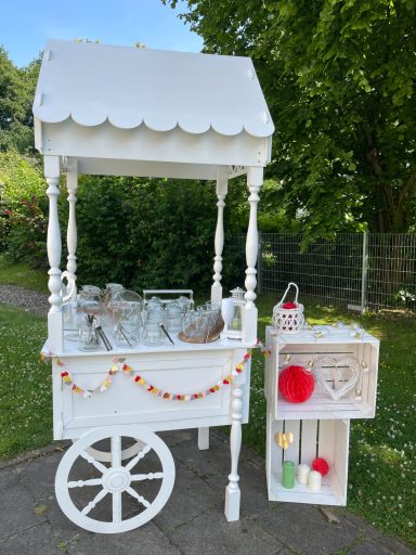 Ein weißer Partysstand Weißer Verkaufsstand im Freien mit Gläsern und bunten Dekorationen.
