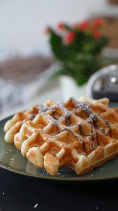 Waffel auf einem Teller, garniert mit Schokoladensauce und frischen Beeren.