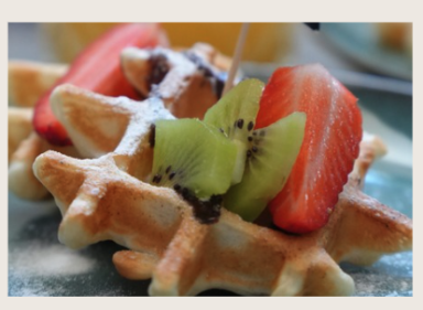 Waffeln serviert mit frischen Erdbeeren und Kiwi, garniert mit Puderzucker.