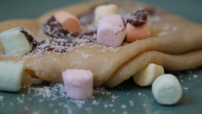 Eine gefaltete Crêpe mit bunten Marshmallows und Kokosraspeln.