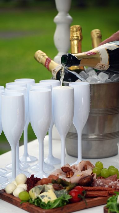 Fingerfood und Sekt Champaigntropfen in Gläser gegossen, umgeben von einer Auswahl an Snacks und Getränken.